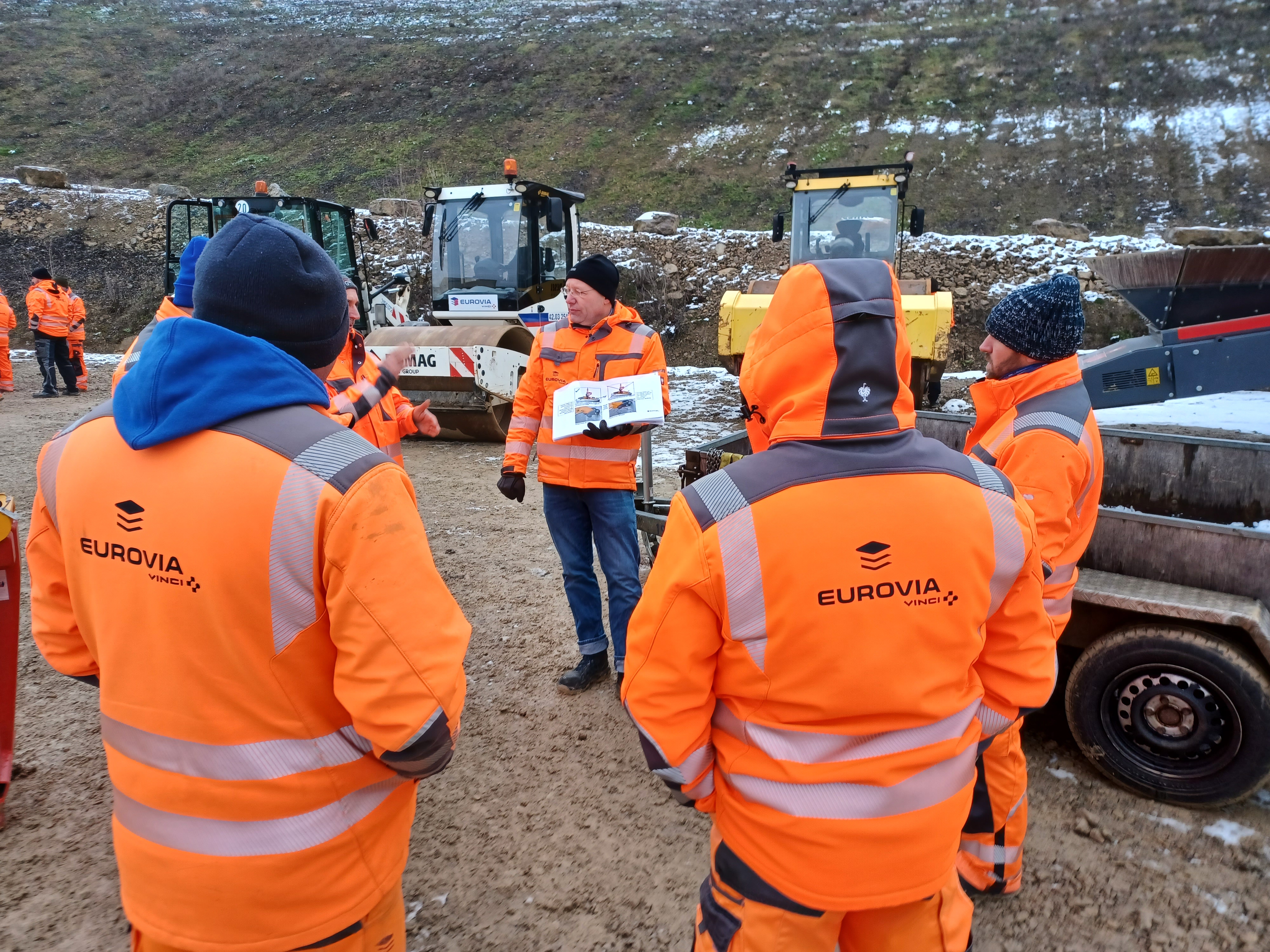 Mitarbeiter stehen im Kreis für die Prestart-Besprechung auf der Baustelle. 