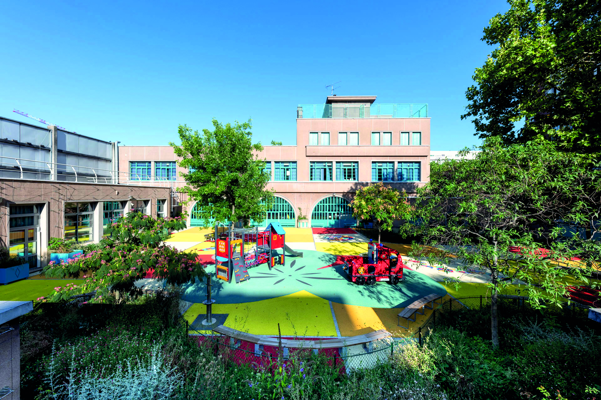 Spielplatz umgeben von Bäumen, mit einer Schule im Hintergrund.