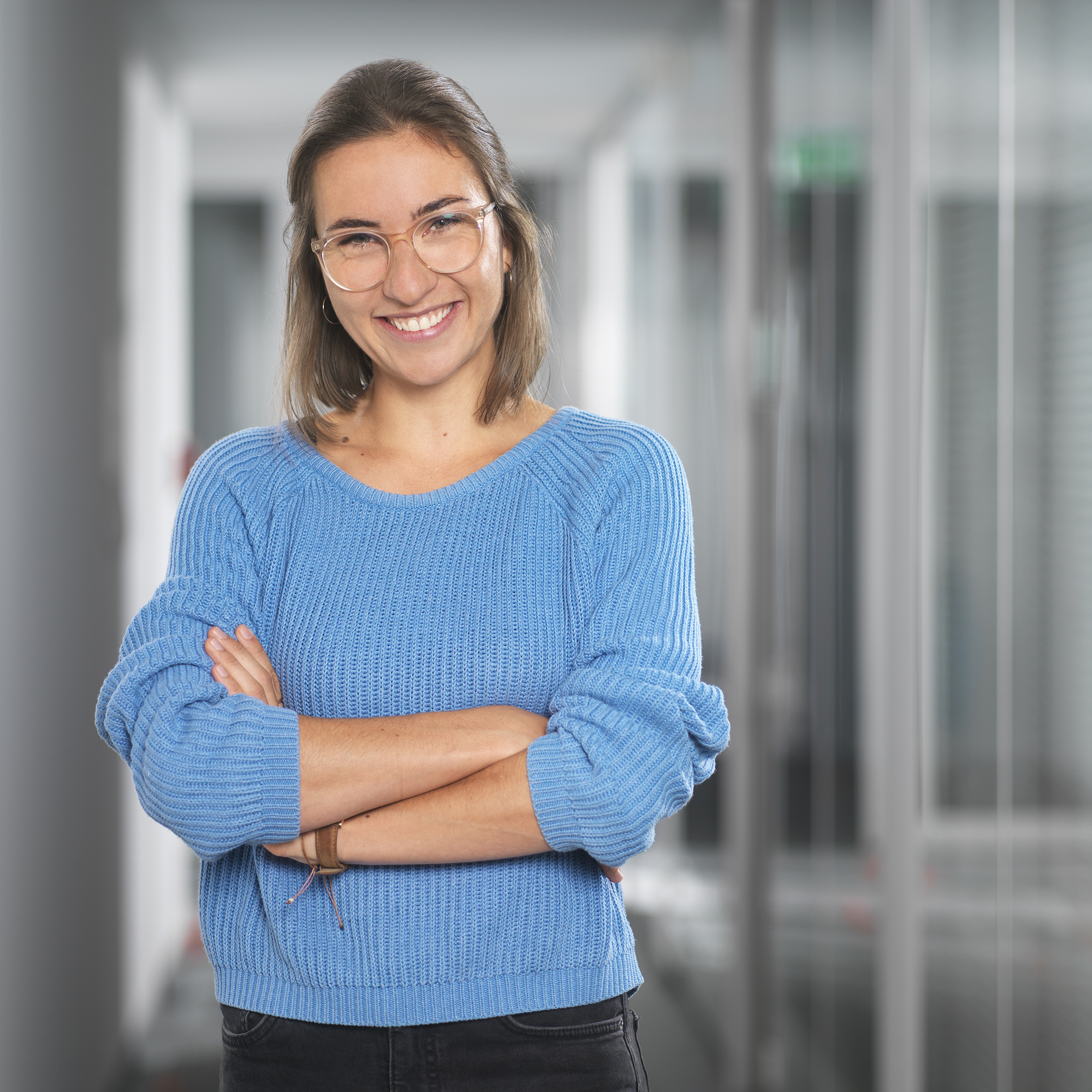 Frau im hellblauen Pullover verschränkt die Arme vor dem Oberkörper.