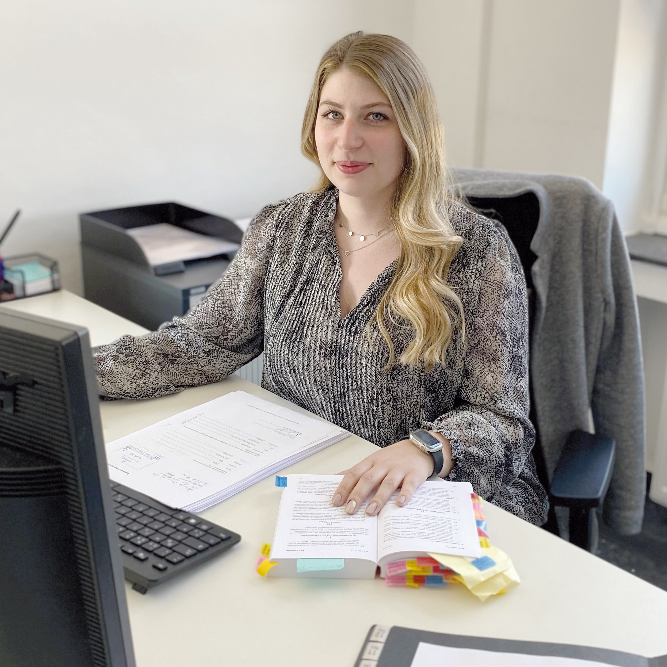 Frau mit blonden langen Haaren, die am Schreibtisch sitzt.