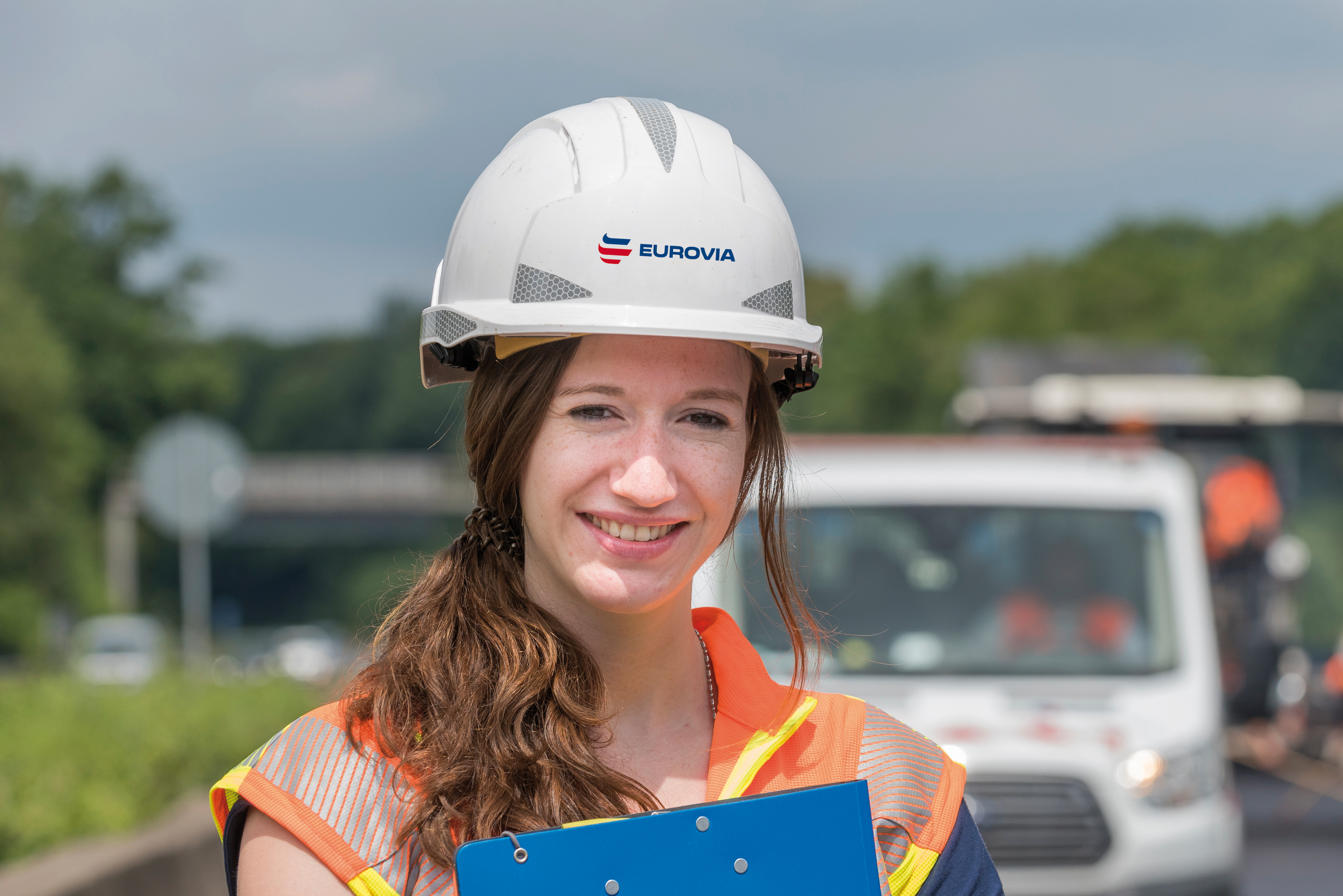 Frau mit weißem Helm und blauem Klemmbrett vor dem Oberkörper.