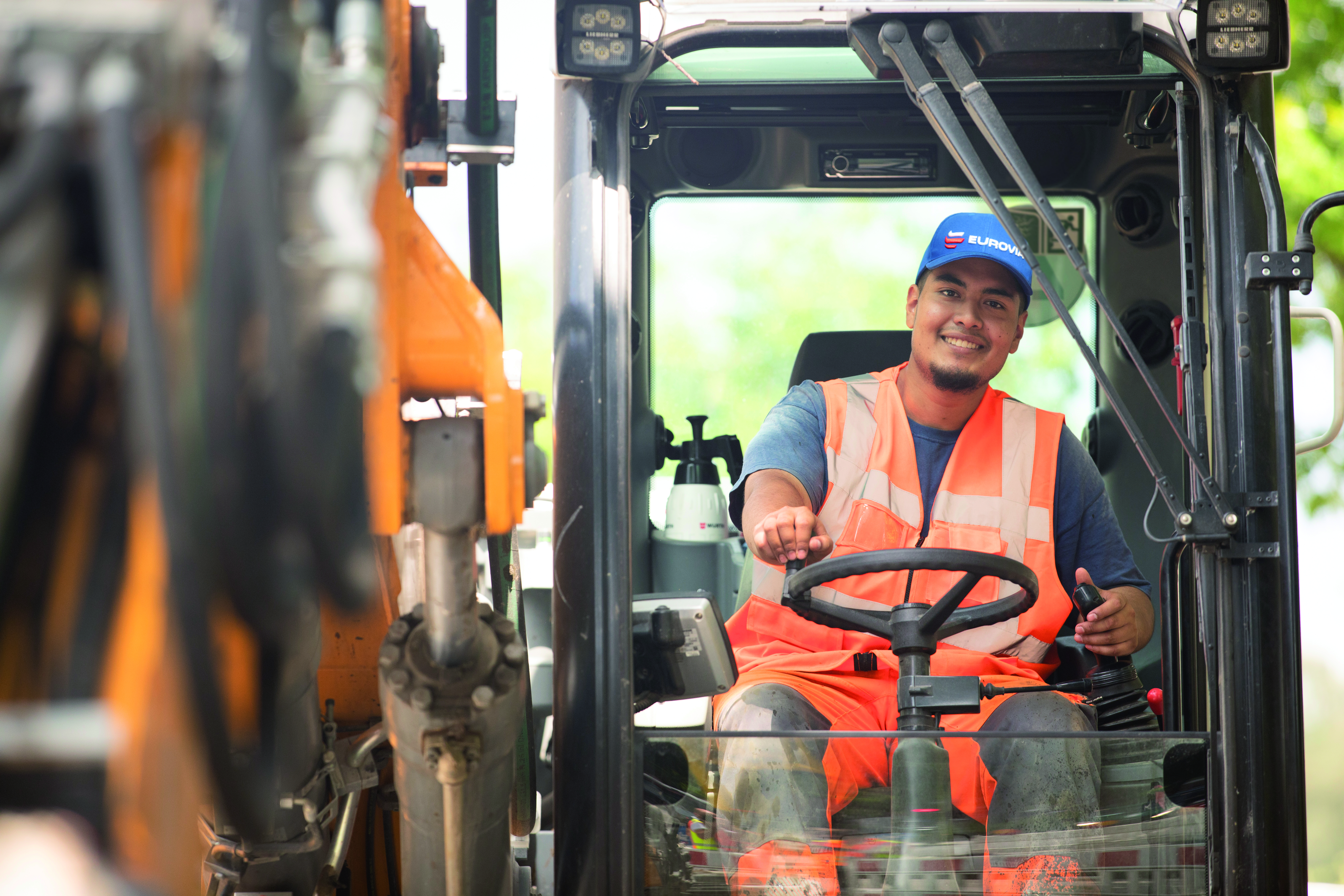 Ein Mitarbeiter fährt einen Bagger und schaut lächelnd in die Kamera.