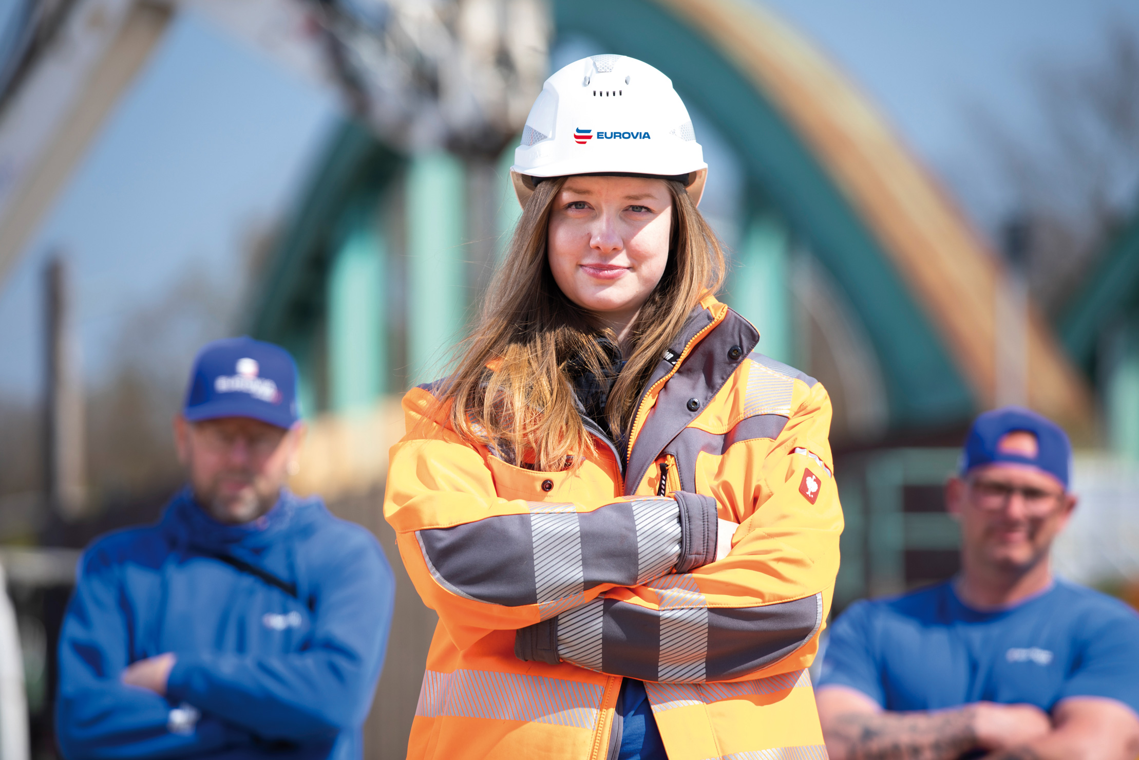 Frau trägt einen EUROVIA-Helm und persönliche Schutzausrüstung (PSA) und hat die Arme verschränkt.