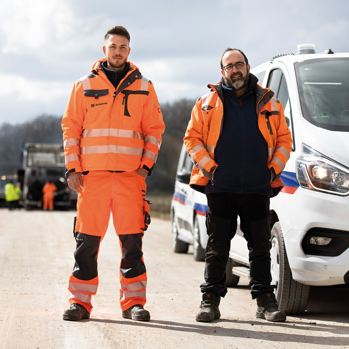 Zwei Männer stehen frontal. Einer trägt eine PSA-Jacke und -Hose, der andere nur eine PSA-Jacke und normale Kleidung.