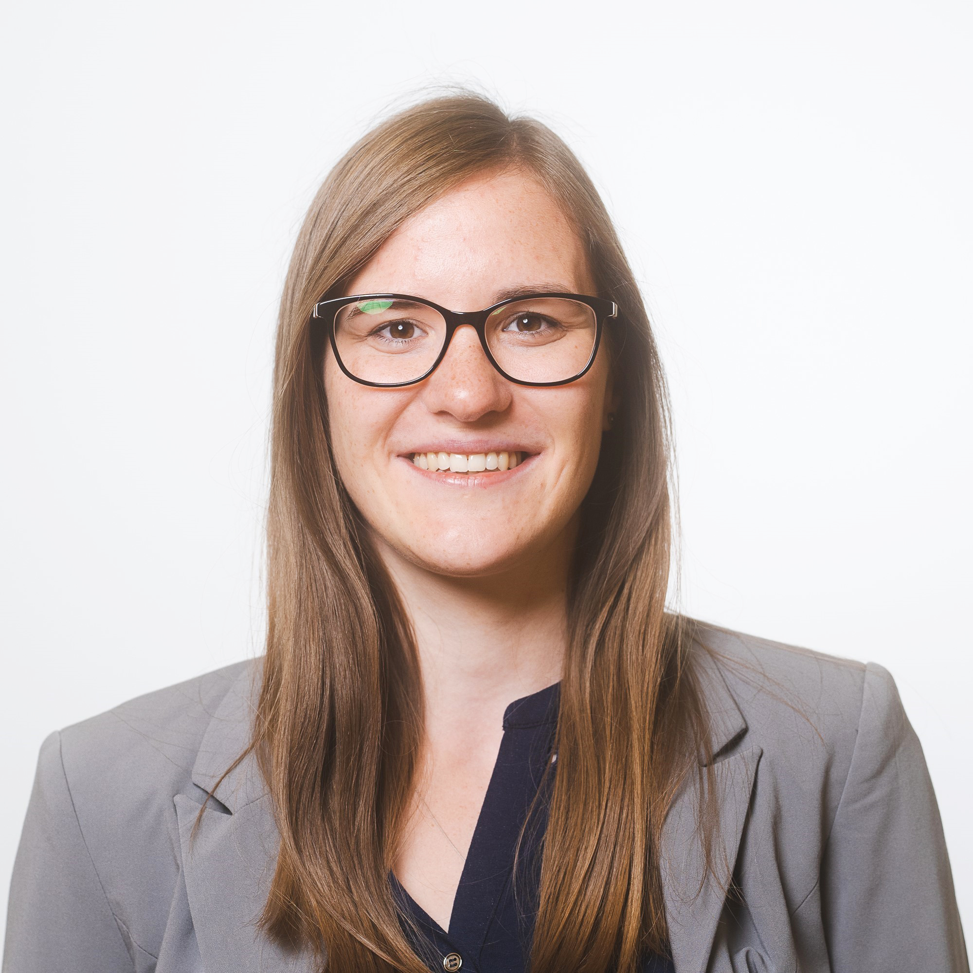 Frau mit Brille und grauem Blazer schaut frontal lächelnd in die Kamera.