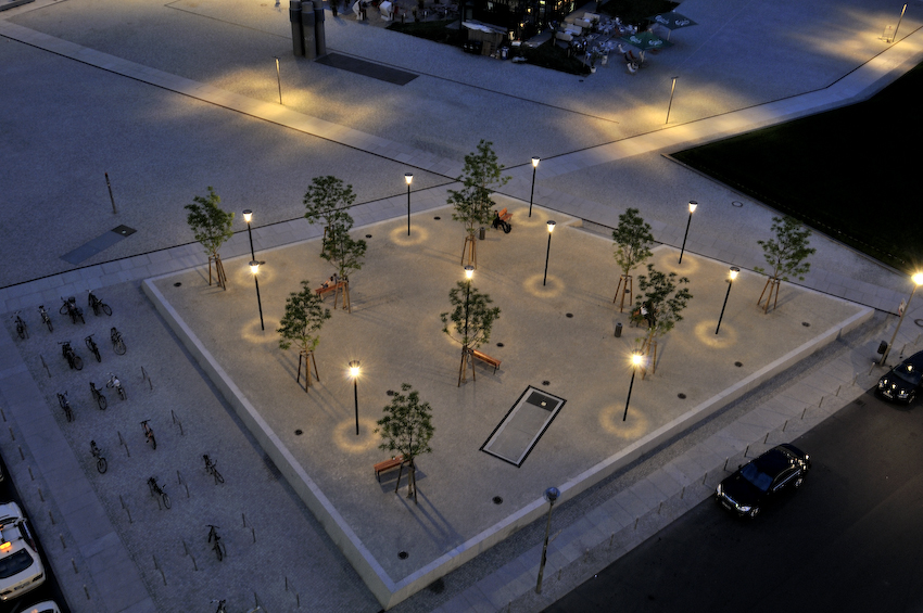 Parkanlage von oben, mit Lichtern, Bänken und einigen Bäumen.