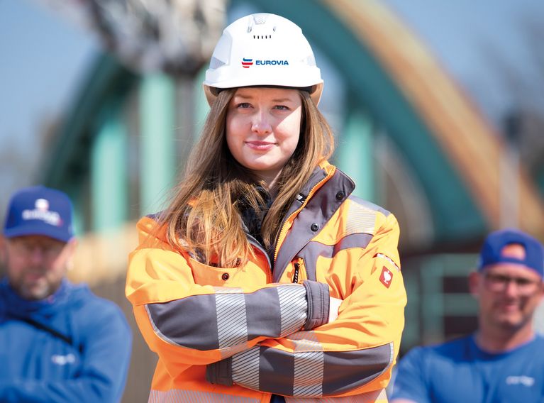 Frau trägt einen EUROVIA-Helm und persönliche Schutzausrüstung (PSA) und hat die Arme verschränkt.